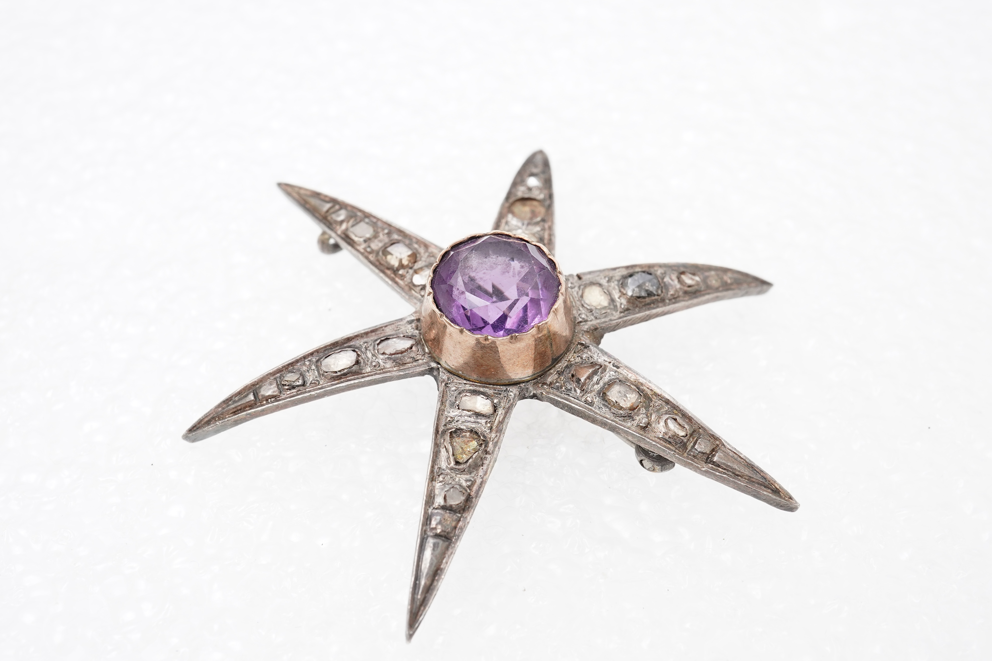 An amethyst and diamond brooch, designed as a star, set with a circular-cut amethyst and rose-cut diamonds, mounted in silver and gold, length 5.7cm, two diamonds deficient